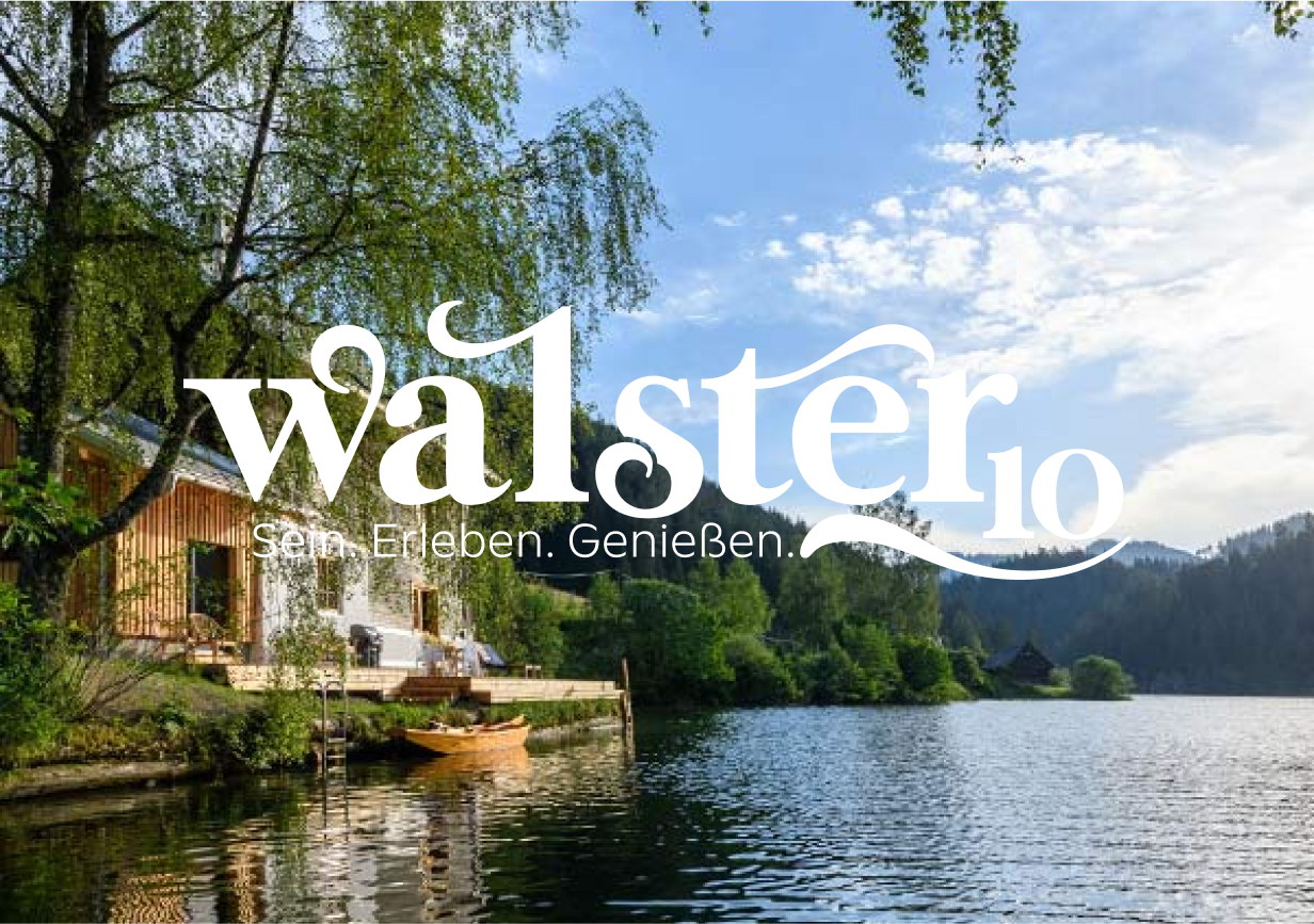 ueber-uns-walster10 Eine Holzhütte am See, umgeben von üppigen grünen Bäumen, mit einem kleinen Boot auf dem Wasser und Bergen im Hintergrund. Der Text walsterio Sein. Erleben. Genießen. ist dem Bild überlagert.
